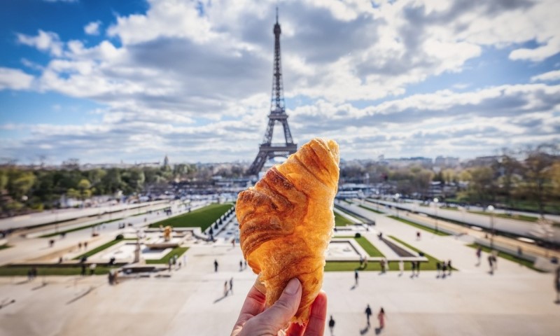 Ruka koja drži francuski kroasan ispred Ajfelovog tornja u Parizu